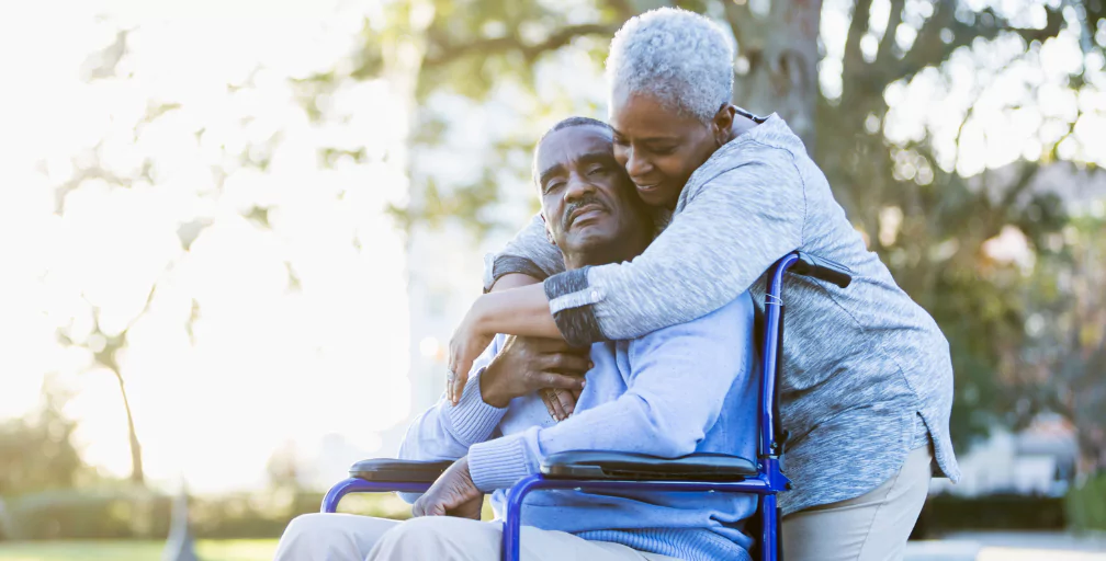 A man sits in a wheelchair in a park and closes his eyes while a woman standing behind him gives him a hug. If you were denied long-term disability benefits in Georgia, talk to Silver & Archibald.