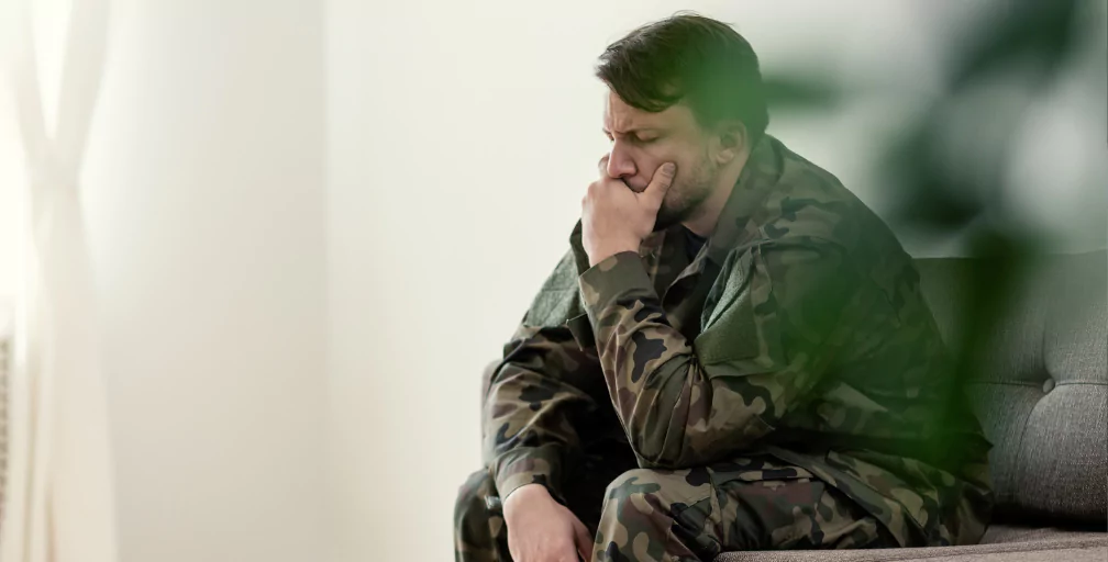 A soldier in fatigues sits on a couch, closing his eyes and resting his chin in his hand. Veterans’ Disability lawyers from Silver & Archibald help Georgians get the maximum benefits.