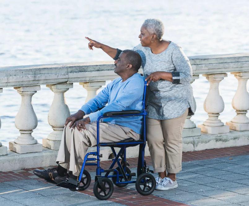By the edge of a body of water, a woman points something out in the distance to the man in a wheelchair who she’s with. Long-term disability policies come in two forms: ERISA and individual.