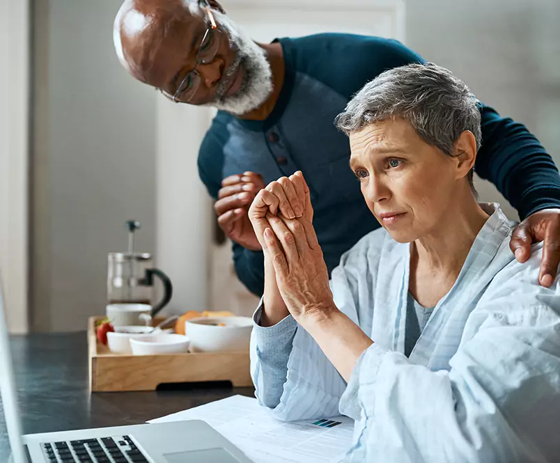 With a concerned expression on her face, a woman puts her hands together and looks at a laptop screen while a man puts his hand on her shoulder. Silver & Archibald lawyers help with Social Security Disability, VA Disability and long-term disability claims