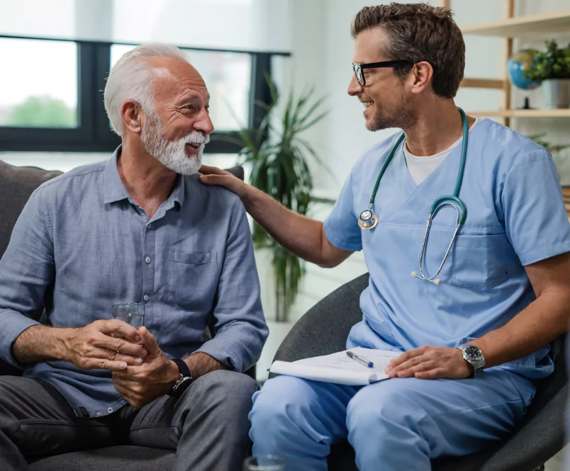 A man sits next to a doctor talking while the doctor puts his hand on the patient’s shoulder. SSD eligibility requires multiple forms of documentation, much of it from doctors.