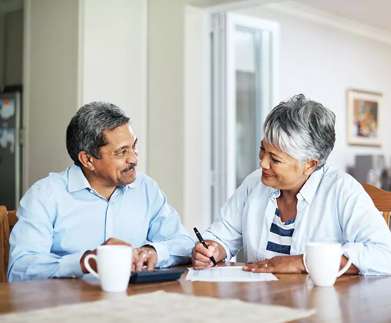 A couple talks at a dining room table with coffee cups, paperwork and a calculator. Social Security Disability attorneys from Silver & Archibald can help you apply or appeal a denial of benefits.
